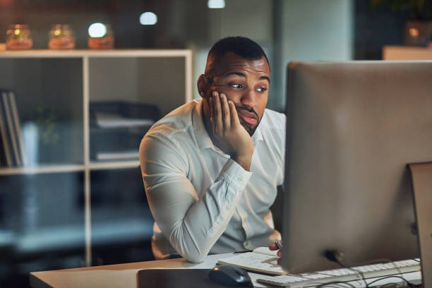 Somebody at a desk, bored, looking at a screen with their head on their hand